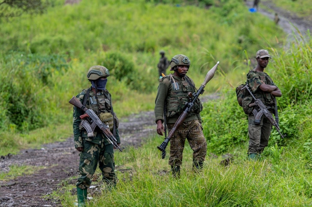 congo-m23-rebels-retreat Armed soldiers stand guard in a field.