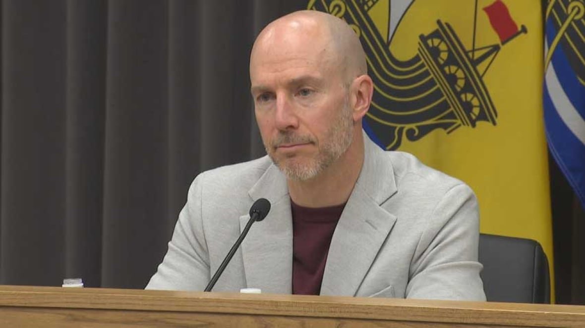 dr-yves-leger-chief-medical-officer-of-health A man wearing a T-shirt and blazer, sitting in front of a microphone, speaking.