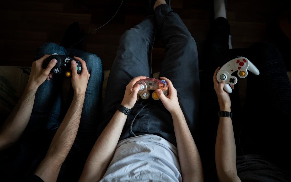esports-gamer The arms of three young men holding video game controllers are seen from above.