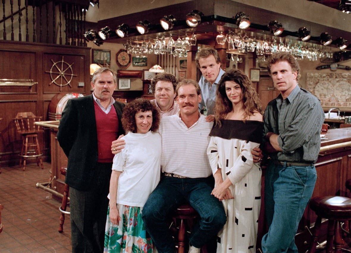 george-wendt-cheers-cast-wade-boggs A group of peole stand together in front of a bar on the set of the TV show Cheers.