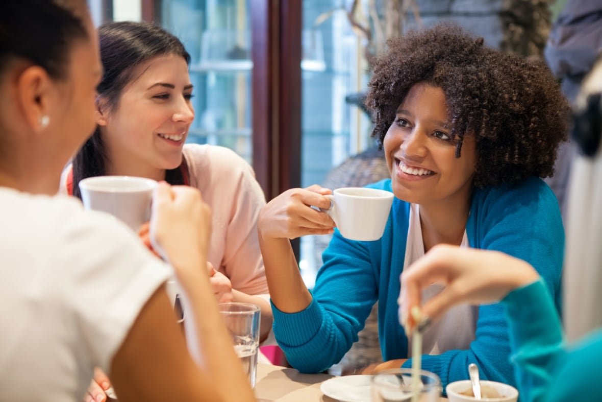 gossip A group of smiling women sit around a restaurant table drinking from mugs.