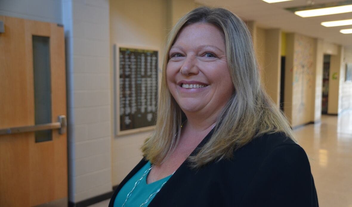 A smiling blonde-haired woman standing in a school hallway