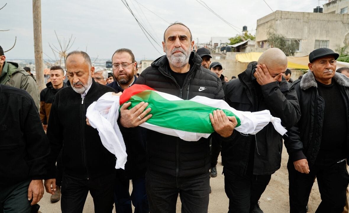 israel-palestinians-jenin-funeral-1 A man carries the body of a toddler wrapped in a Palestinian flag, followed by other men dressed in black.