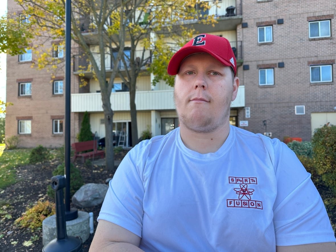 kale-mcmurren A man wearing a baseball hat stands in front of an apartment building.