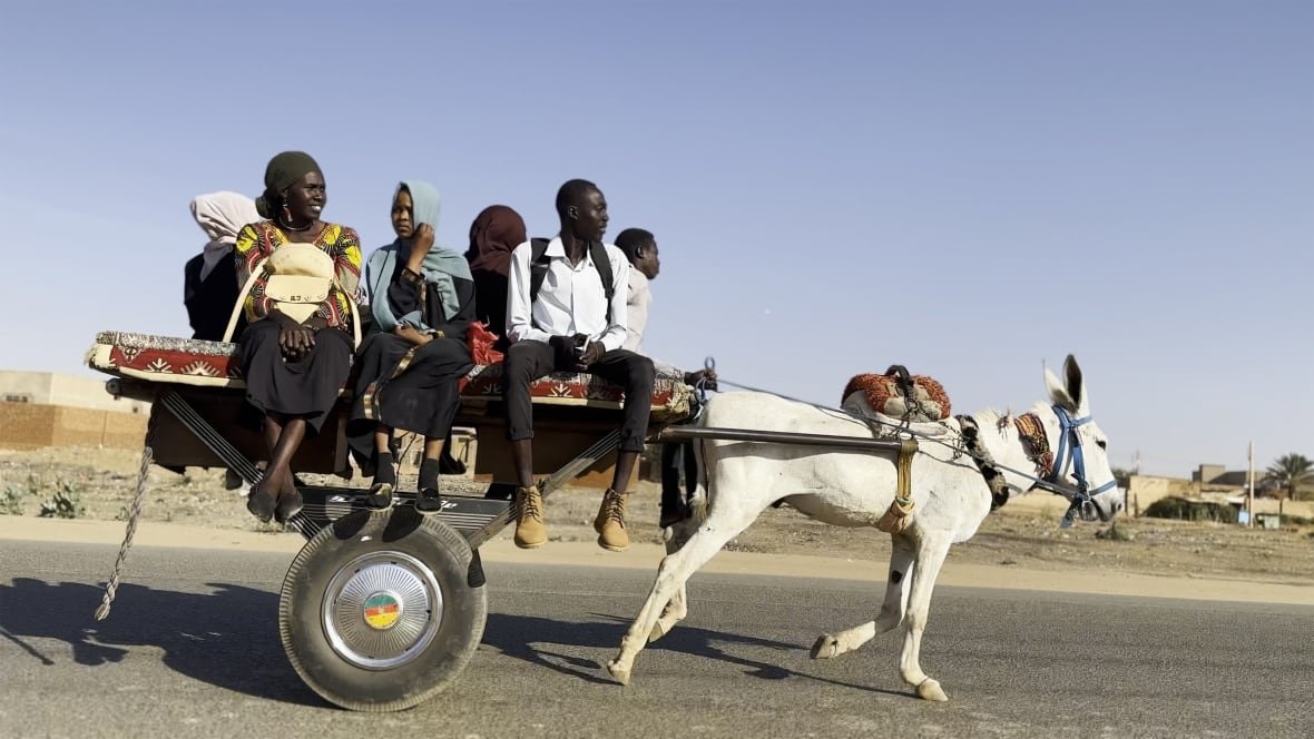 khartoum A group of people sit on a wheeled cart being pulled by a donkey.