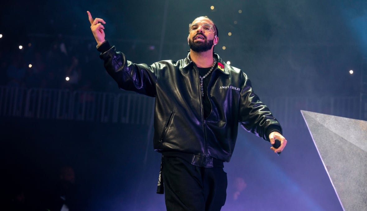 music-drake-tour-20241125 A man stands onstage, with one hand lifted up, finger pointed, in the middle of talking or singing.