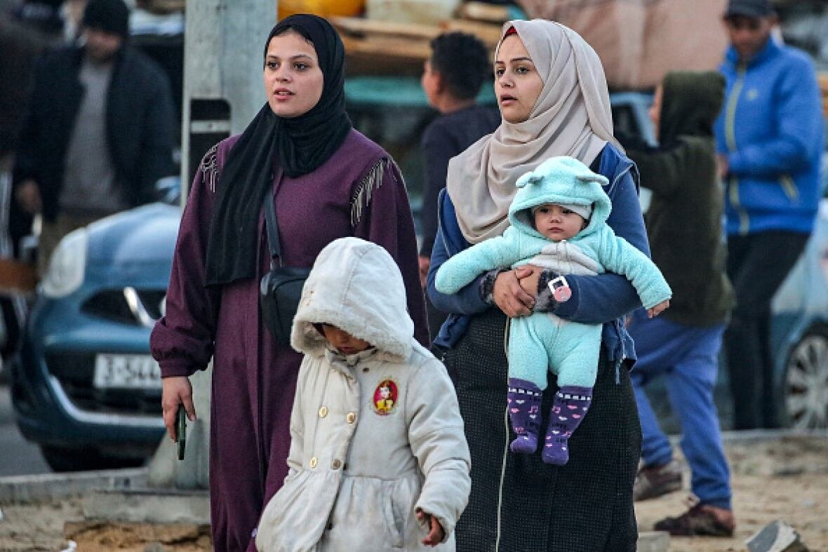 northern-gaza Two women walk along along a road with a young child. One carries a baby.