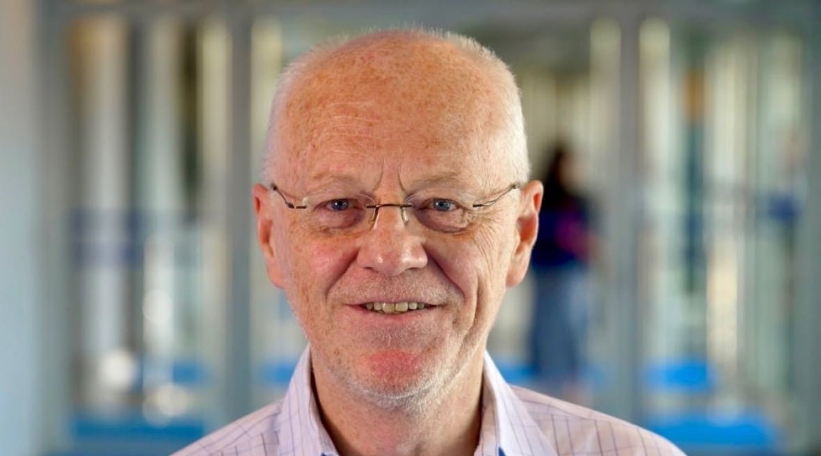 peter-goadsby Balding, smiling man wears glasses and a purple shirt with stripes.