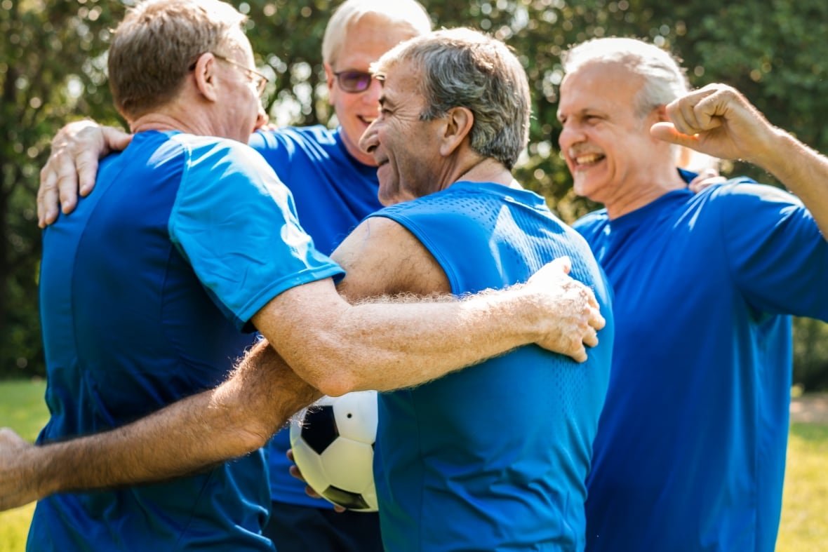 shutterstock-huge-file A group of senior men playing soccer on a sunny day gather close in celebration.