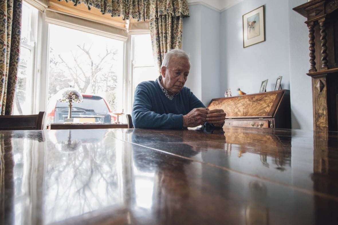 shutterstock-medium-file-2 Senior man is sitting alone at the dining table in his home, with a worried expression on his face.