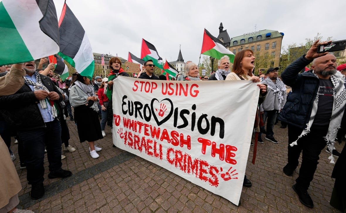 sweden-eurovision-israel A crowd of protesters carries a large sign that says "Stop Using Eurovision to Whitewash Israeli Crimes". Many Palestinian flags are visible.