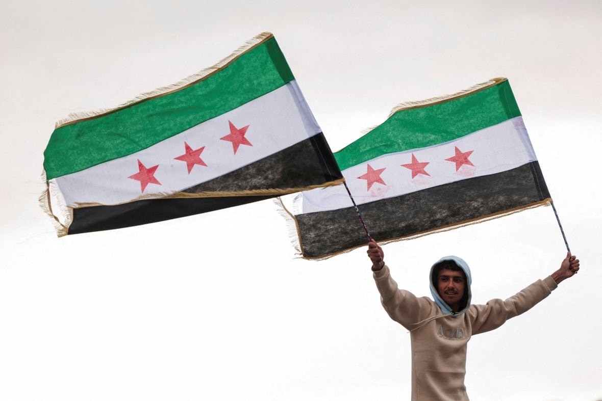 syria-security-egypt A person holds flags adopted by the new Syrian rulers.