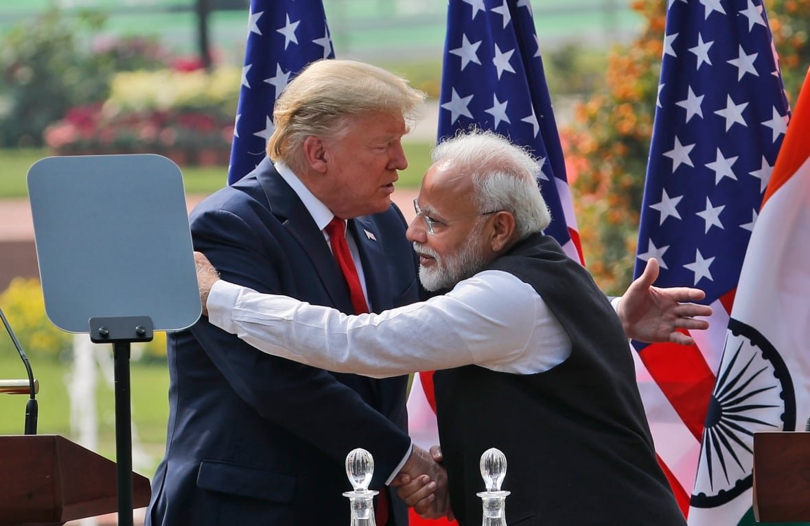 us-election-2024-india A balding, bearded man with glasses wearing a vest and shirt hugs a cleanshaven man in suit and tie.
