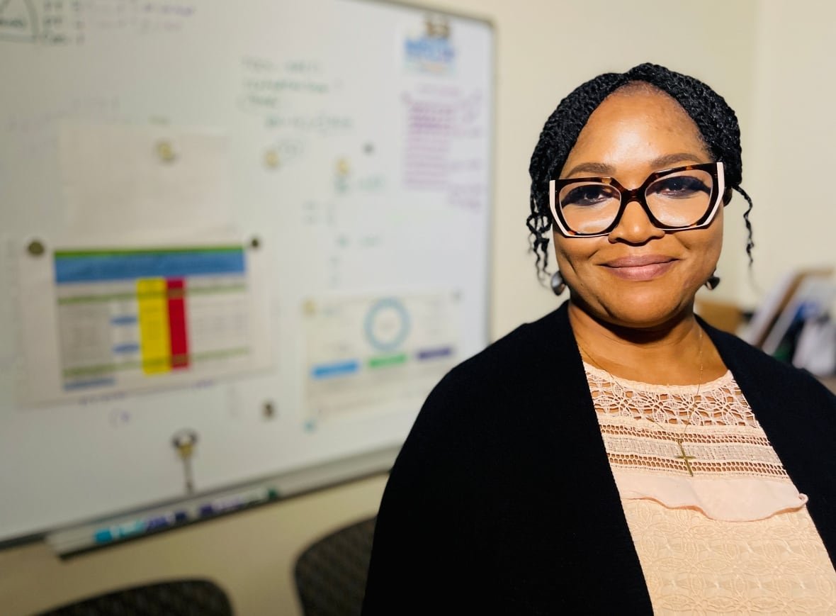 vickie-idowu A woman wearing glasses, peach blouse, black cardigan and a crucifix, smiles.