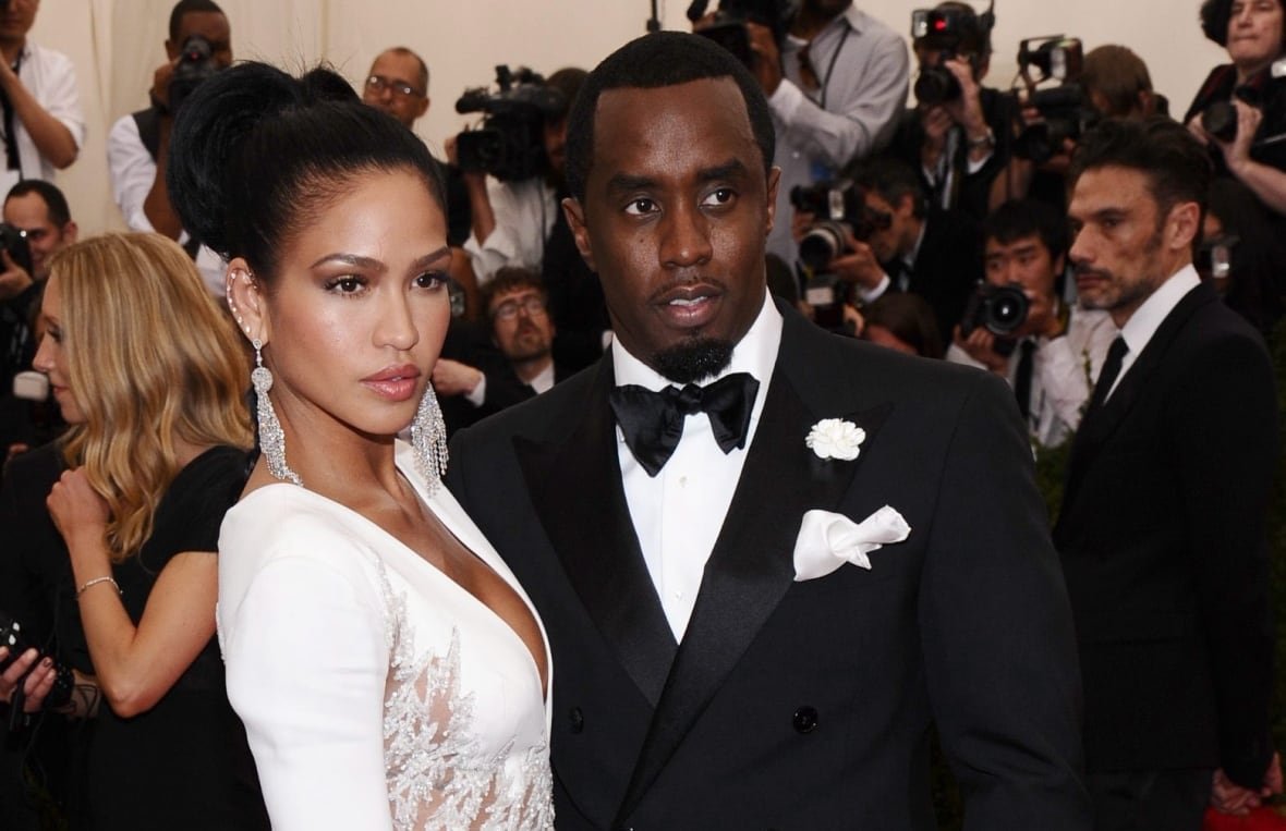 2015-met-museum-costume-institute-benefit-gala-1 A man and a woman pose together on a red carpet. They are shown from the waist up and are posing turned in towards each other, looking out. The man is in a black suit an the woman is in a white, long-sleeved dress.
