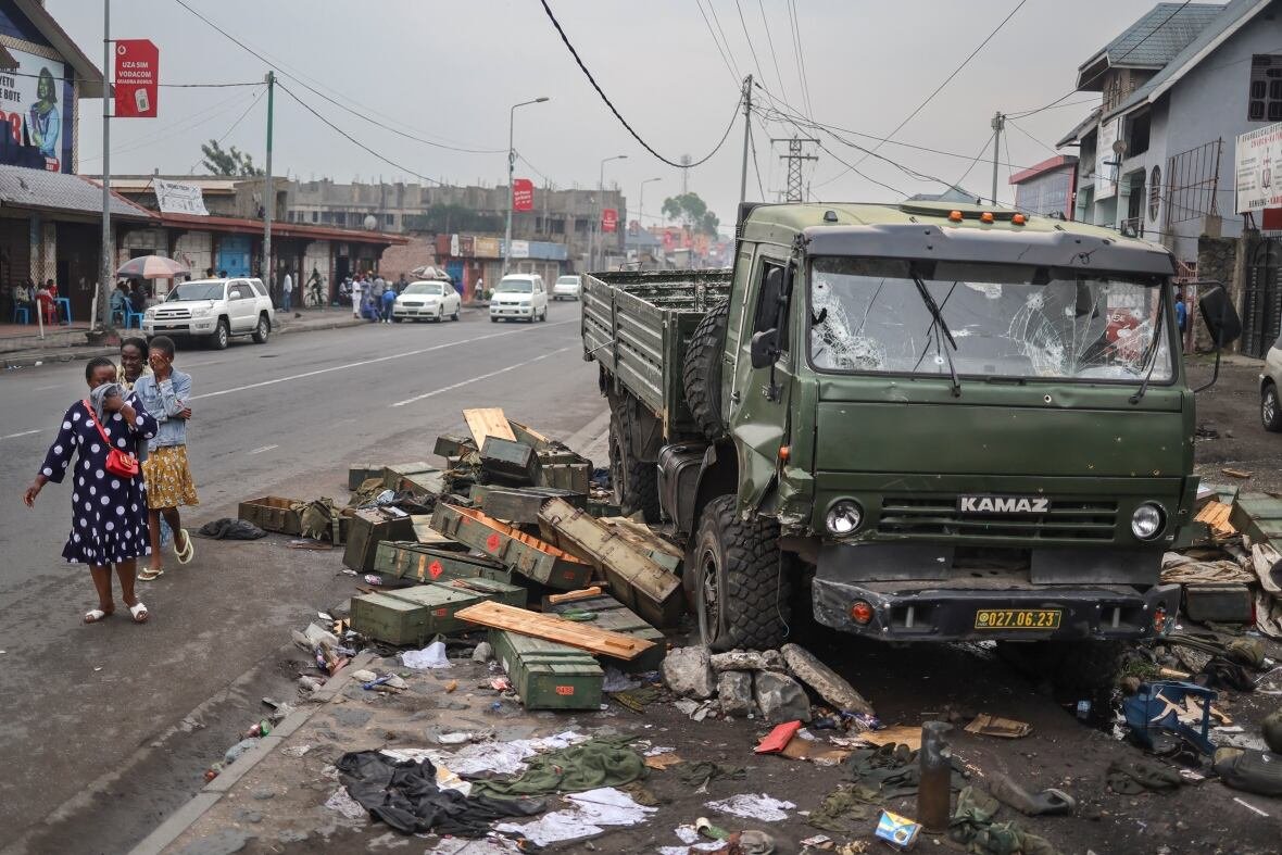 People cover their faces as they walk past a bullet-riddled military vehicle.