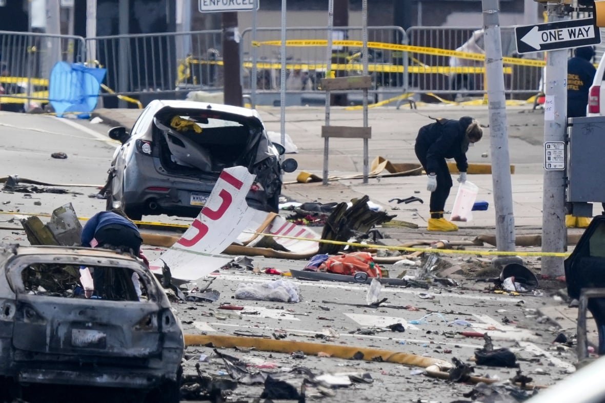 A person collects aircraft wreckage on the street near damaged cars.