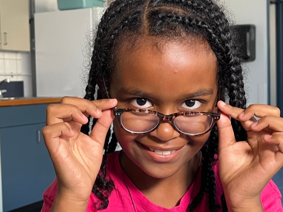 betel-kelem A young girl smiles as she adjusts glasses on her face.