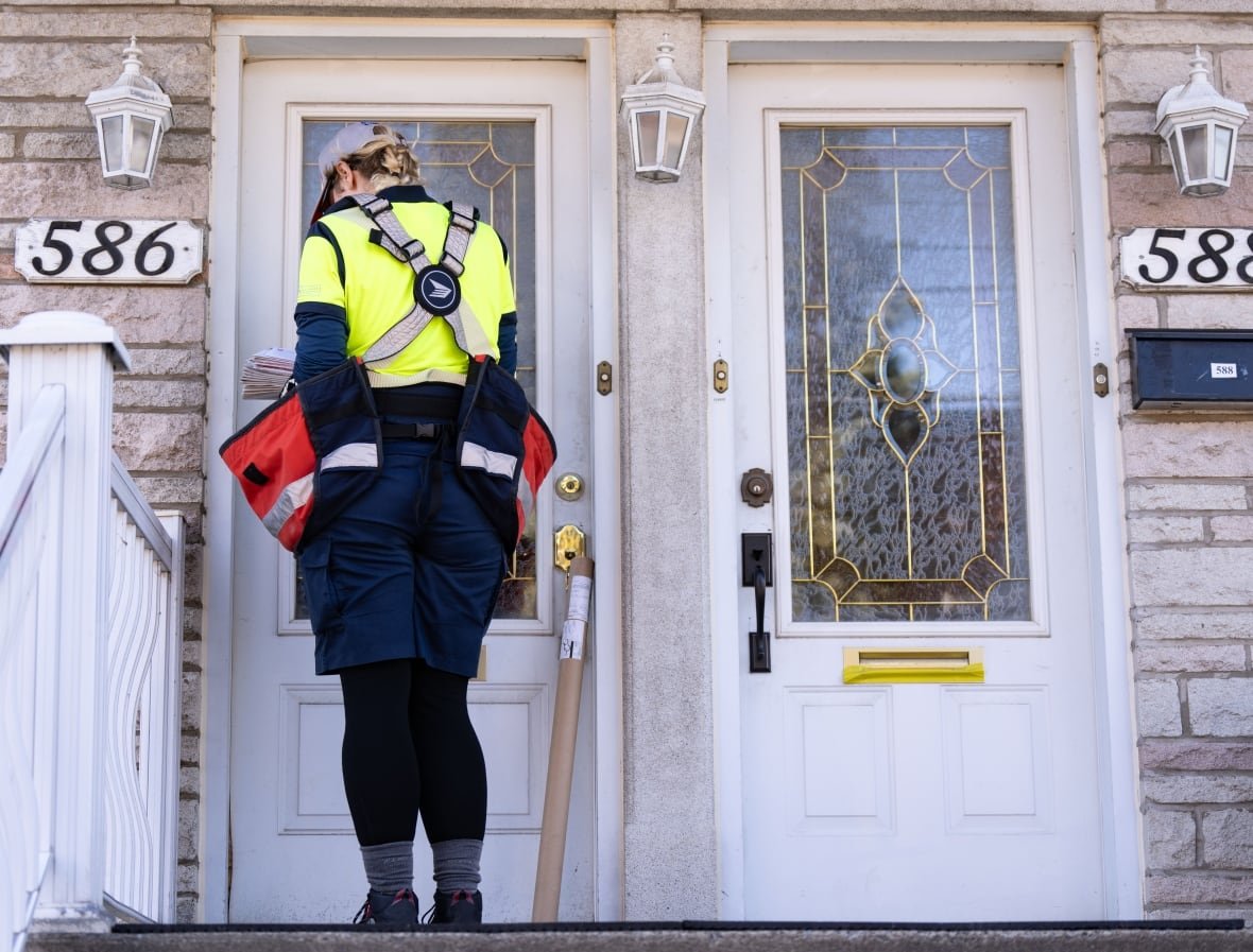 canada-post-strike-20241113 A mail carrier delivers a package to a front door.