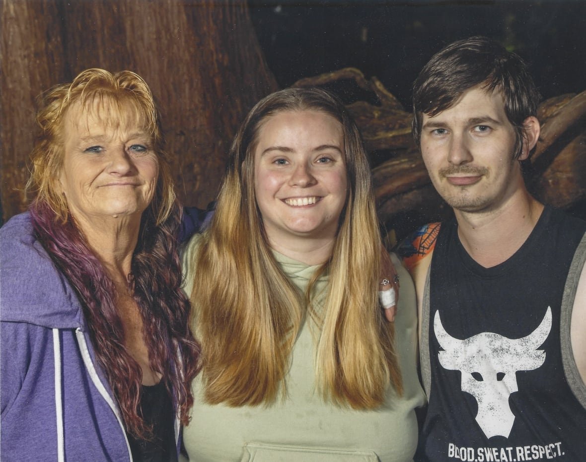 diane-chandler-and-children An older woman with red hair at the left of the picture smiles beside a young man and a woman who are also smiling.