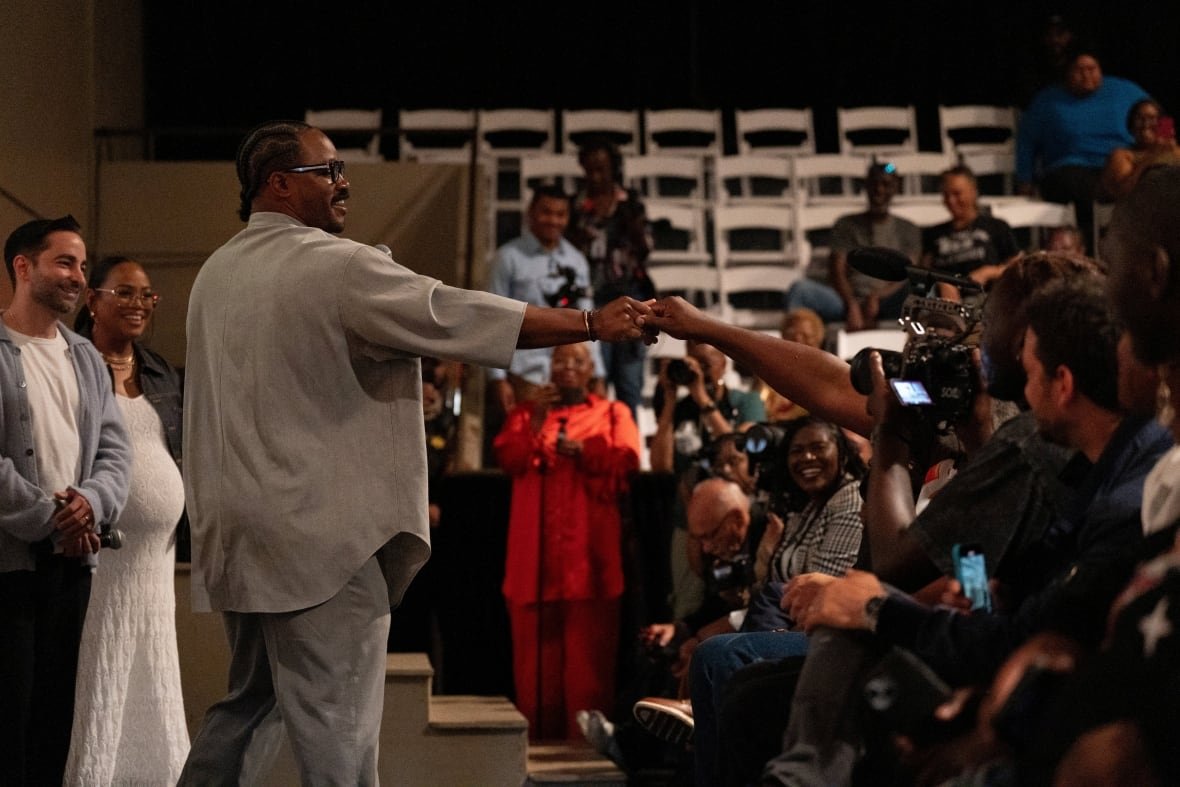 film-sinners-mississippi-2 A man on stage fist-bumps an audience member in a crowded auditorium