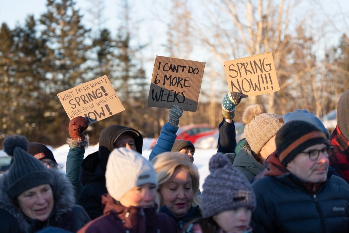 groundhog-day-canada-20250202 A crowd standing outside on snow holds signs protesting winter and calling for spring to come.
