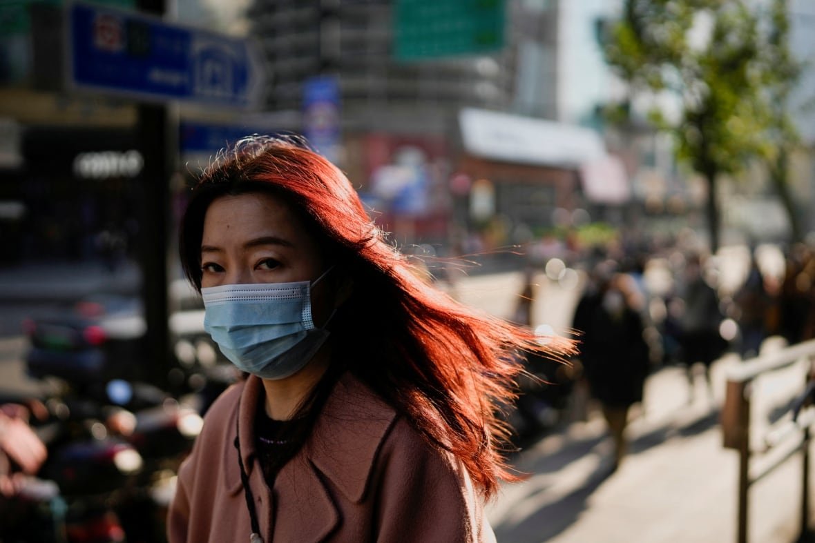 health-coronavirus-china A woman with long hair wearing a face mask and coat walks on a street in Shanghai, China.
