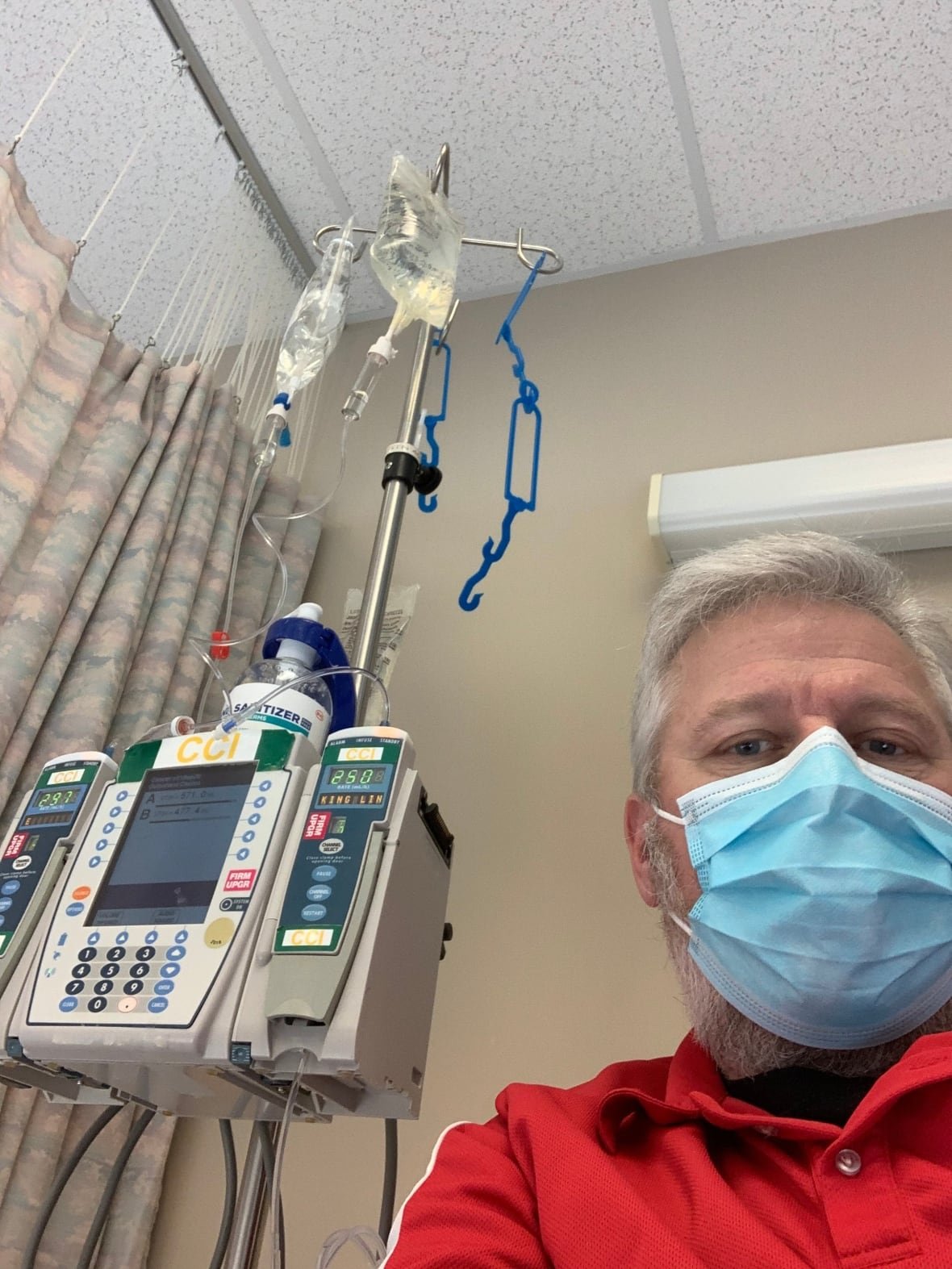 james-smith-at-the-hospital A man wearing a surgical mask next to medical equipment.