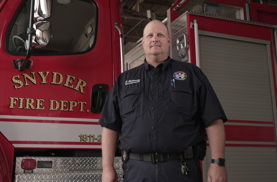 jay-callaway A man in a dark blue uniform next to a firetruck.
