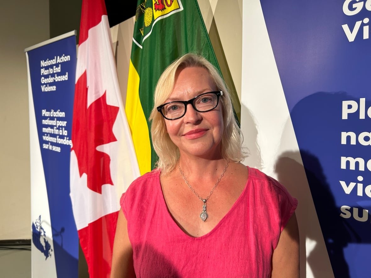 jo-anne-dusel A woman in pink dress stands in front of Canada's flag.