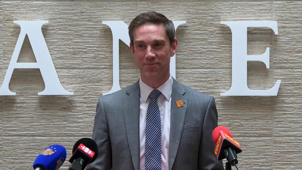 john-hogan-1 A smiling man wearing a suit stands at a podium.