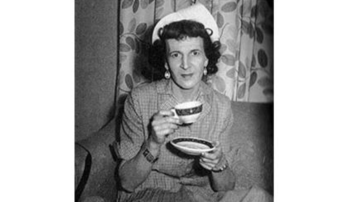 louise-lawrence A black and white photo shows a woman holding a teacup in one hand and a saucer in the other.