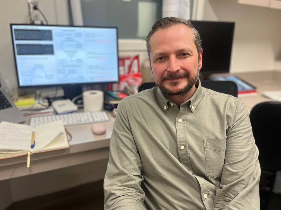 nathan-spreng A bearded man sitting in front of a computer monitor wearing a light coloured, button-down shirt.
