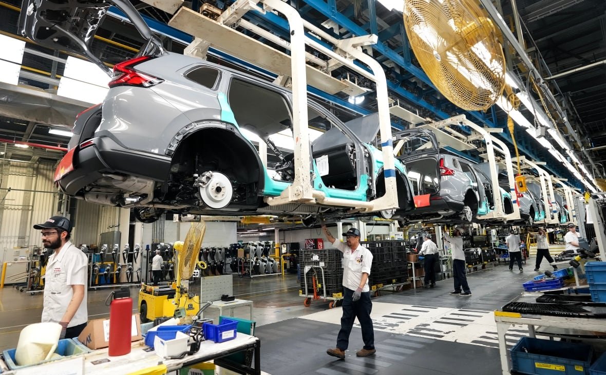 ont-honda-evs-20240425 Workers in an automotive plant walk along a car assembly line.