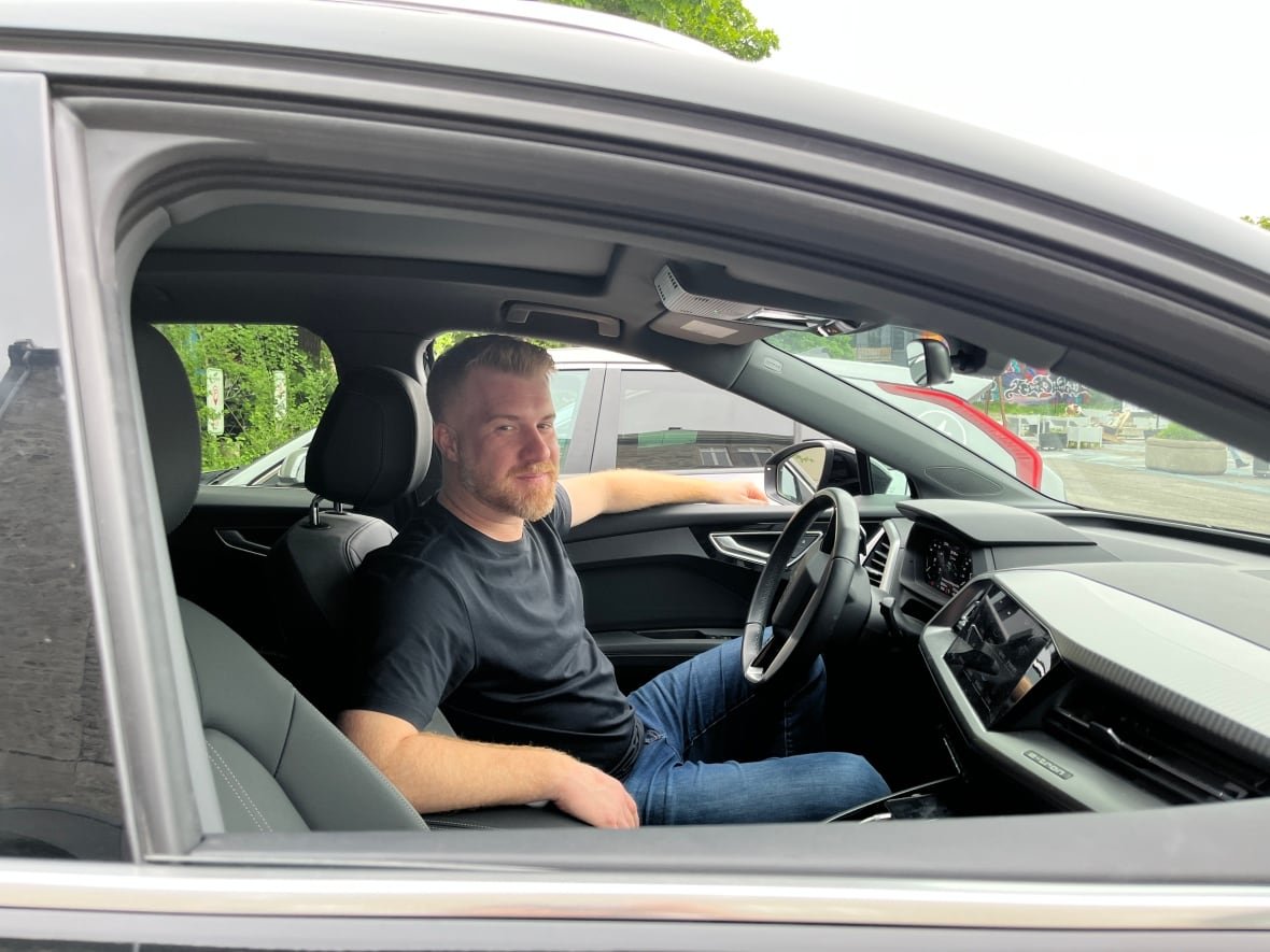 philippe-bergeron-belanger A man with red hair sits in a black car and smiles through the open window.q