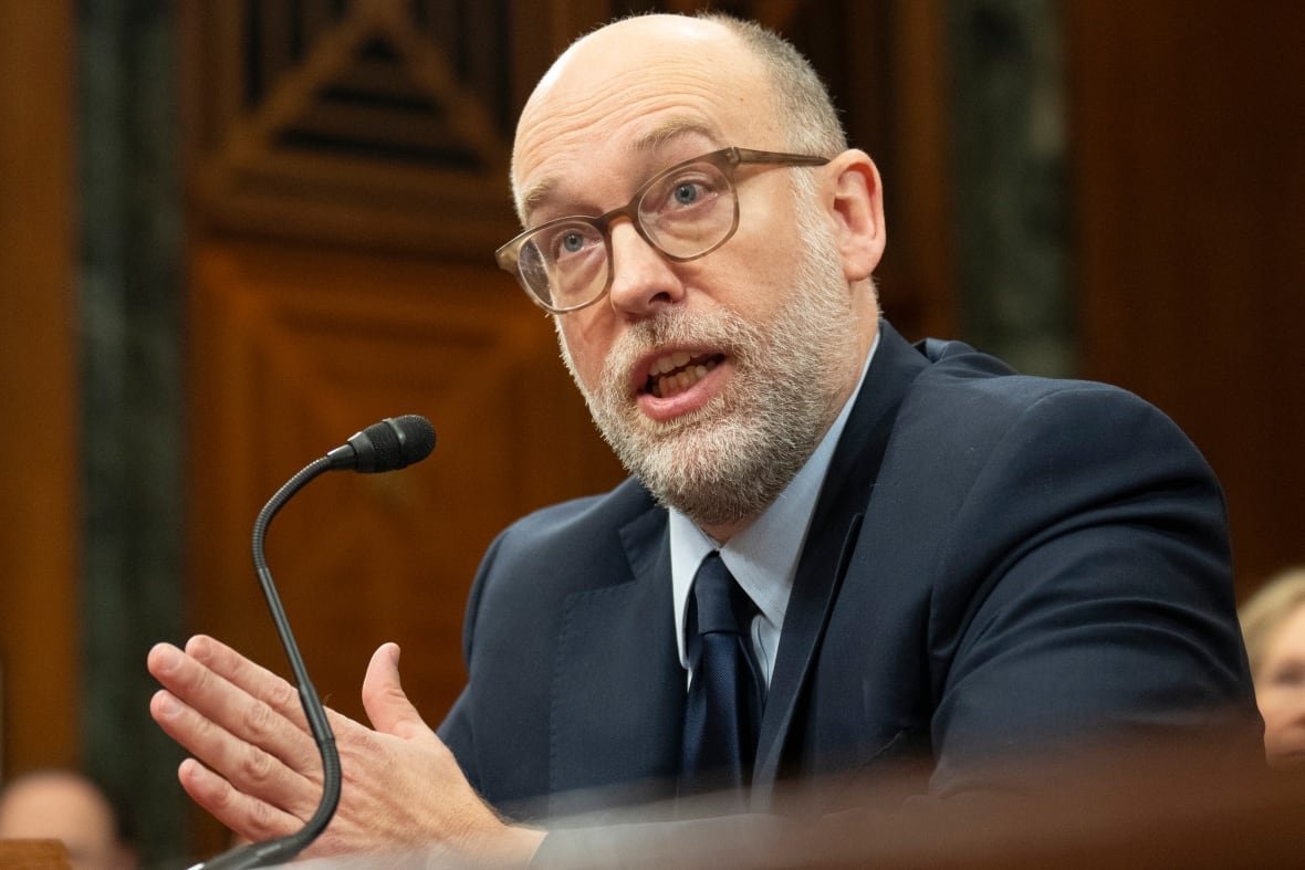 senate-budget A bearded, balding man is shown in closeup speaking into a microphone while seated.