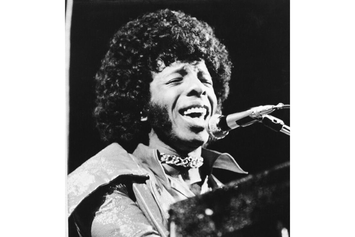 A black and white photo shows a man singing into a microphone.
