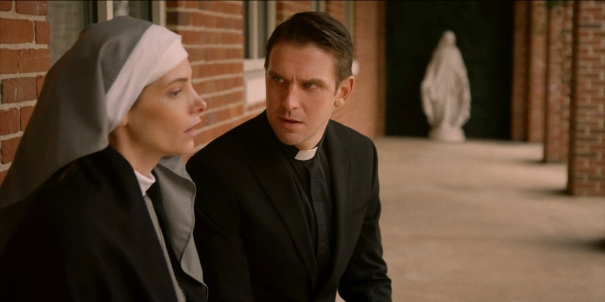 the-ritual-1 A priest speaks to a nun. They are both seated in an outdoor hallway.