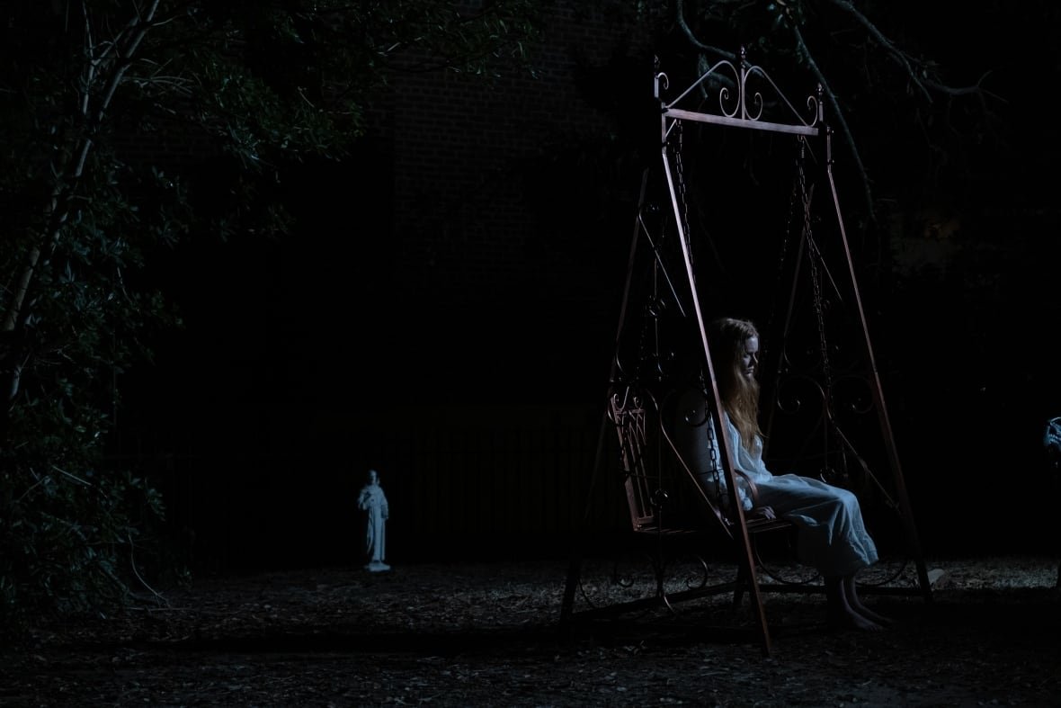 the-ritual-3 A woman sits on a swing in the dark.