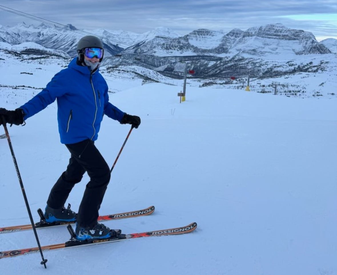 thomas-flannery-skiing A man in skis poses for a photo on a snowy ski hill with a mountain range visible in the background.