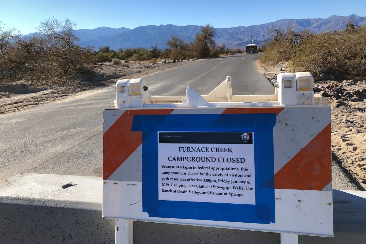 usa-shutdown-parks A closed sign is shown by a road that is surrounded by a rural area, with mountains shown in the background.