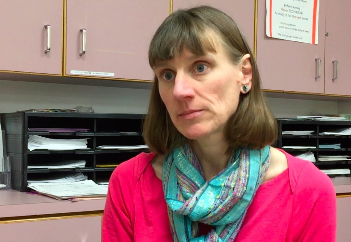 vivien-suttorp-ahs A woman with brown hair looks off camera. She's wearing a bright pink shirt and turquoise scarf. Files can be seen stacked on shelves behind her.