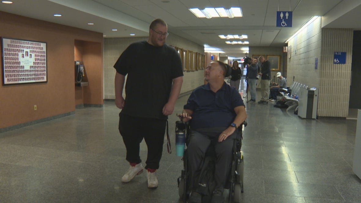 claude-labelle-1 a man in a motorized wheelchair in a courthouse hallway, with his son walking beside him