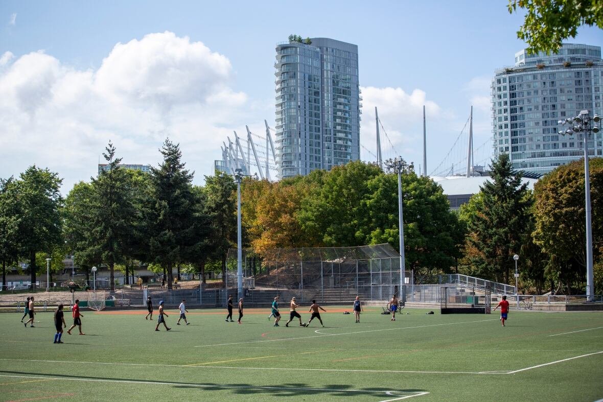 crosstown-neighbourhood-andy-livingstone-park People play soccer near a large stadium on a sunny day.