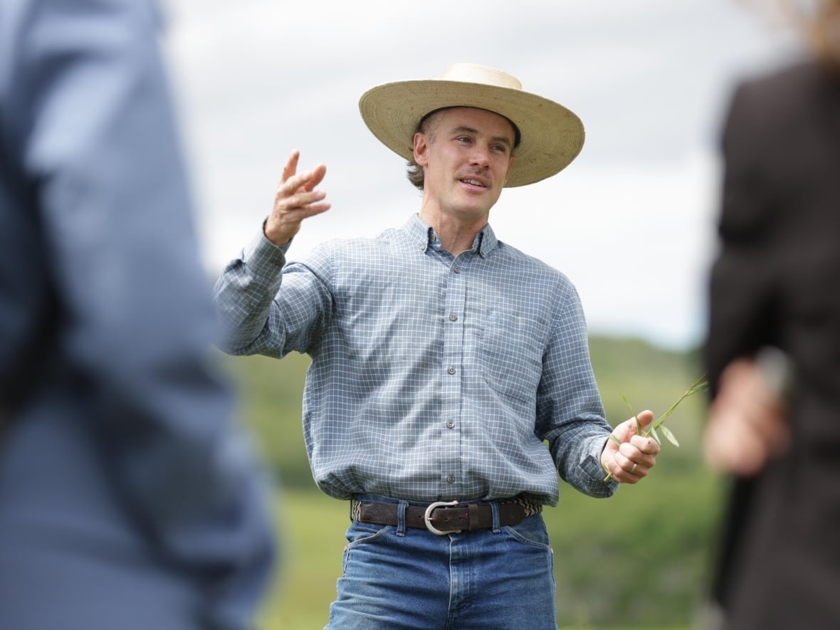 A man speaks to an audience while standing in a field.