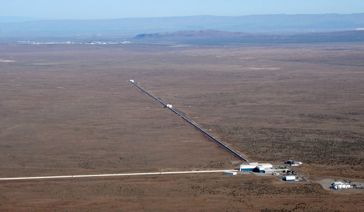 ligo-hanford A building with two long metal arms stretch into an empty, dusty landscape.