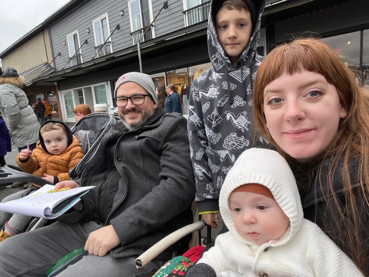 sarah-paquin-and-family A woman with long brown hair sits outside with three young boys and a bearded man with a toque on.