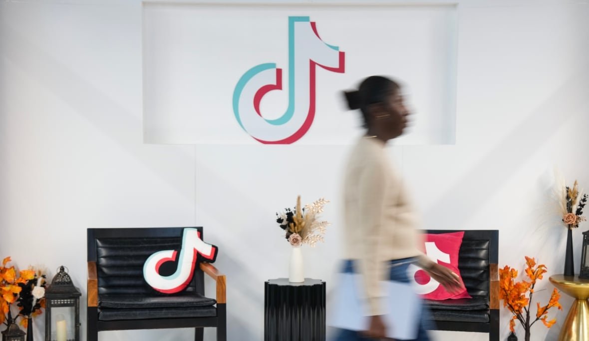 tiktok-ban-20241210 A woman walks by chairs in an office, with the TikTok logo in the background.