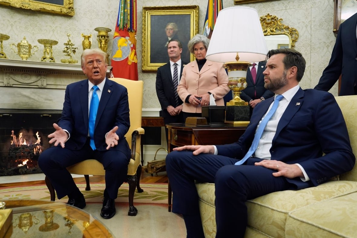 Two people seated in the White House while others stand behind.