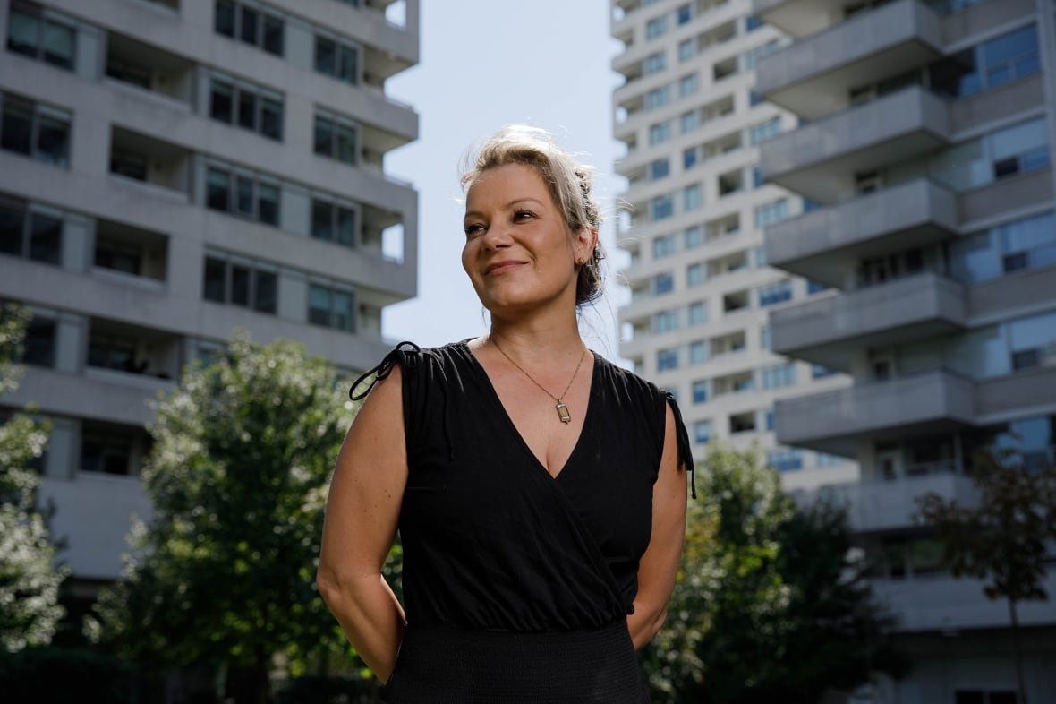 A woman stands on the street, two residential buildings behind her.